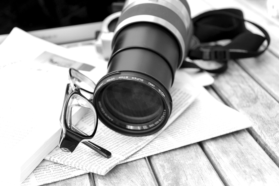 Kameraobjektiv mit Birlle und Zeitung auf einem Tisch